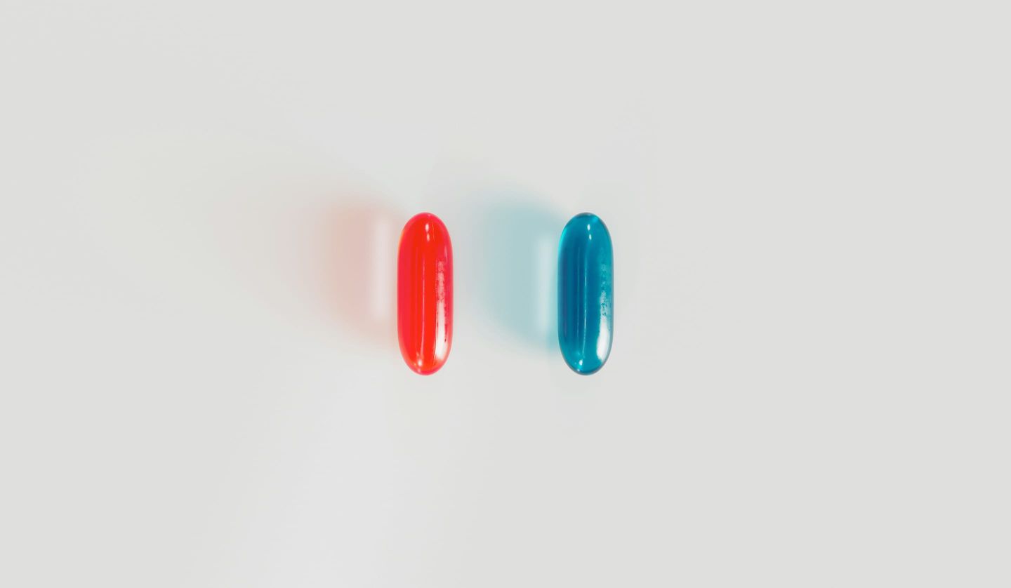 A red pill and a blue pill standing side by side on a plain background